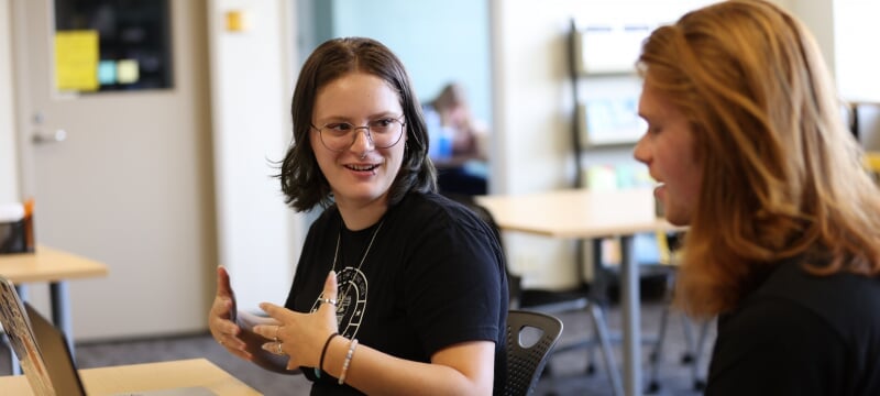 A student writing coach assists a fellow undergraduate student with a writing assignment.
