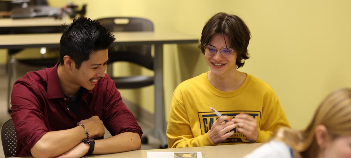 Two first-year writing students laugh while discussing a handout on the desk.