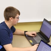 View over the shoulder of instructor Claire Helakoski as she works with a male student at his laptop.