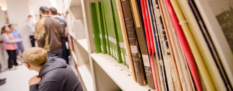 Students leaning up against bookshelves in the library