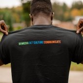 Student holding the back of his shirt up to show that it reads: Do Media Set Culture Communicate