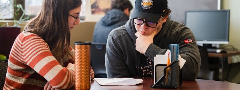 Two students sitting at a table looking over a paper.