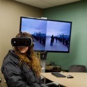 A seated student with a virtual reality headset on in front of a large monitor