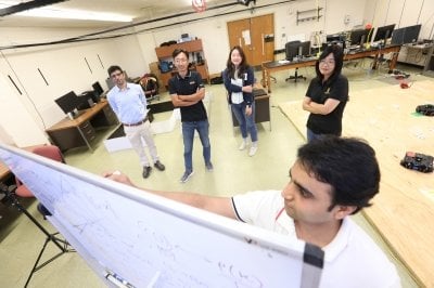 Students and professor gather around a whiteboard