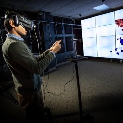 a man with a VR headset looks at an array of monitors