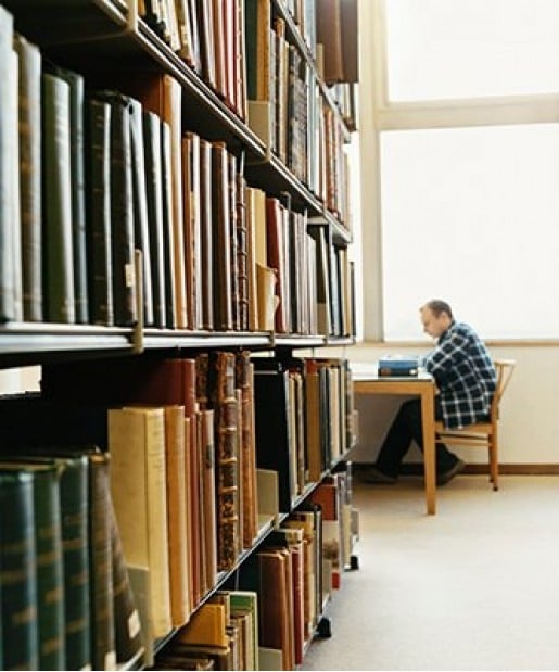 Student sitting at a table past a shelf full of books.