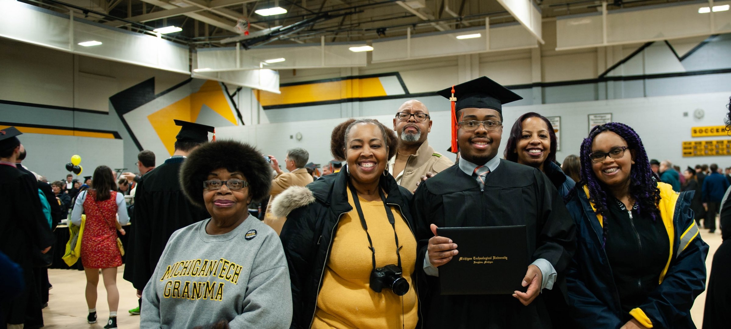 Family of an international student at graduation ceremony posing with commencement plaque