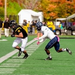 a michigan tech football player carries the ball as an opposing player pursues him