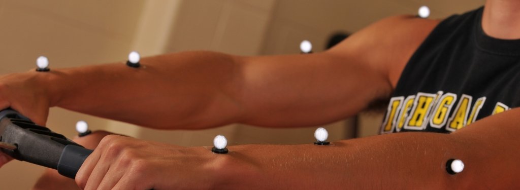 Student on a rowing machine with lighted monitoring devices on his arms and legs