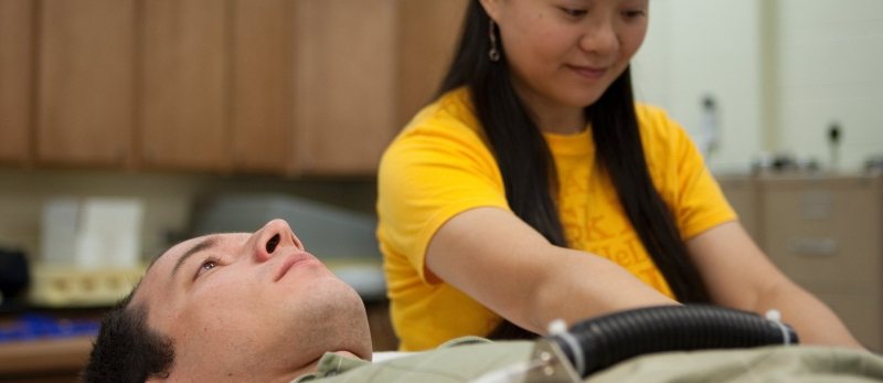 Female researcher adjusting equipment on a male participant who is laying on a table.