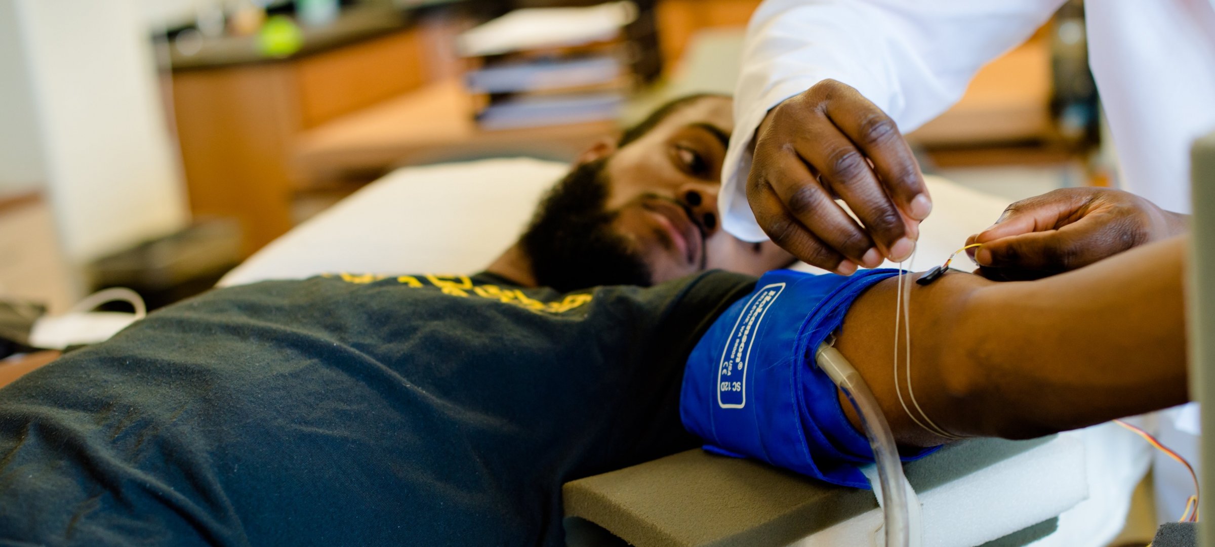 Male laying on table getting his blood pressure monitored and additional monitoring nodes being added.