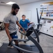 Participant on treadmill with reacher looking on