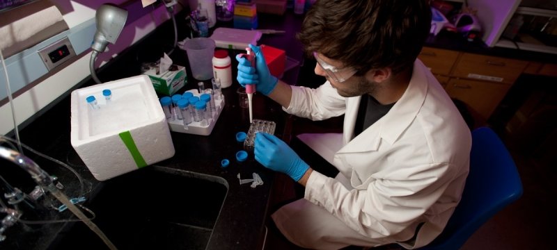 Researcher using a pipet to extract fluid from a vial