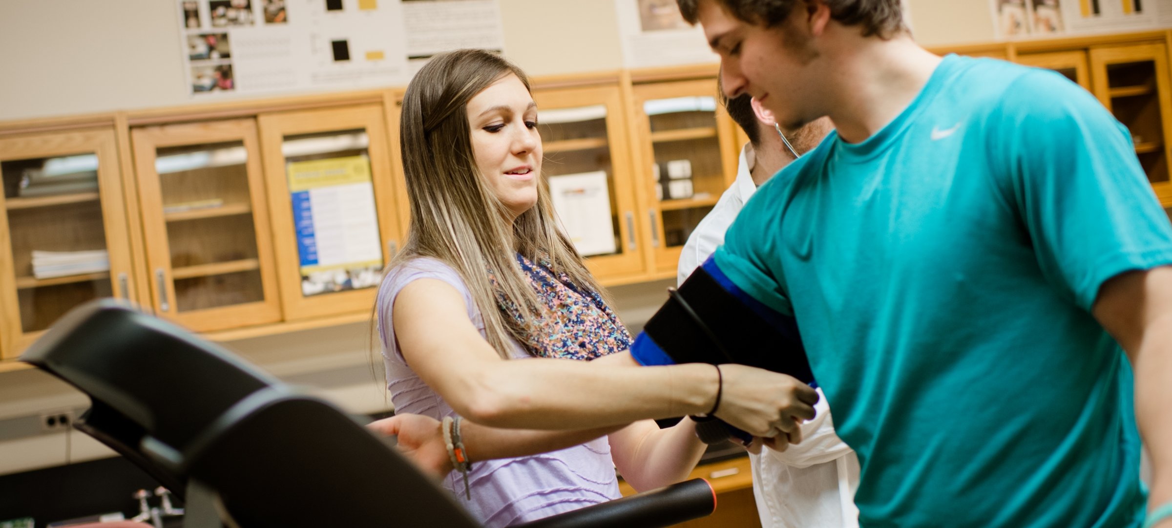 Researcher connects a blood pressure cuff to a student standing on a treadmill.
