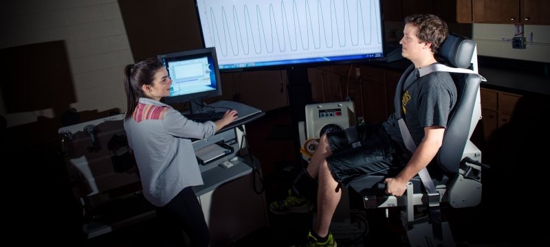 One student standing at a monitor while another is in a chair for testing.
