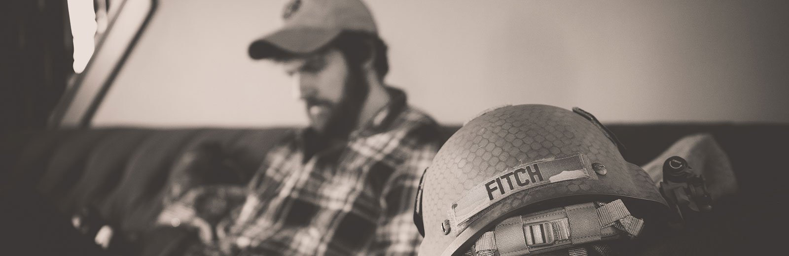 Justin Fitch in the background and his military helmet with his name in the foreground.