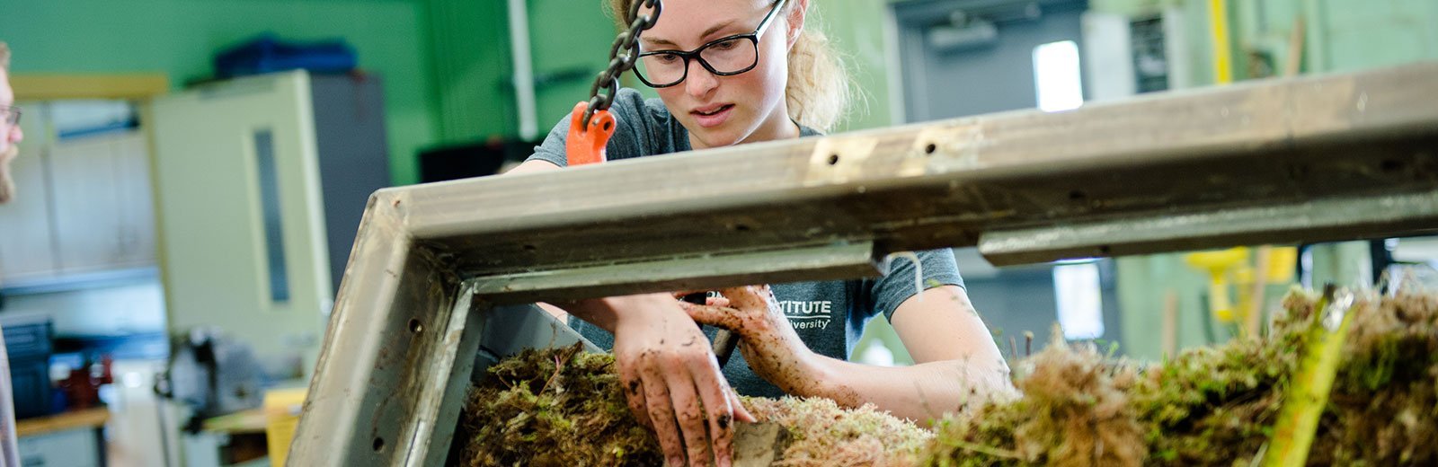 Student cutting samples from a section of peat in a lab.