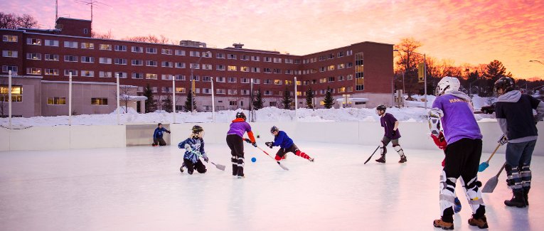 Student playing broomball with Wadsworth Hall and a sunset in the background.