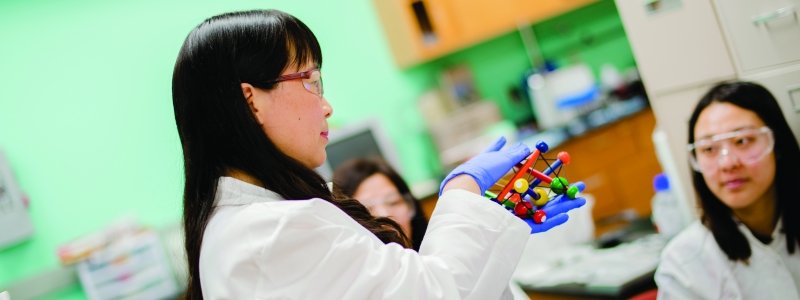 Three researchers in a lab with one holding a model of spheres and sticks.