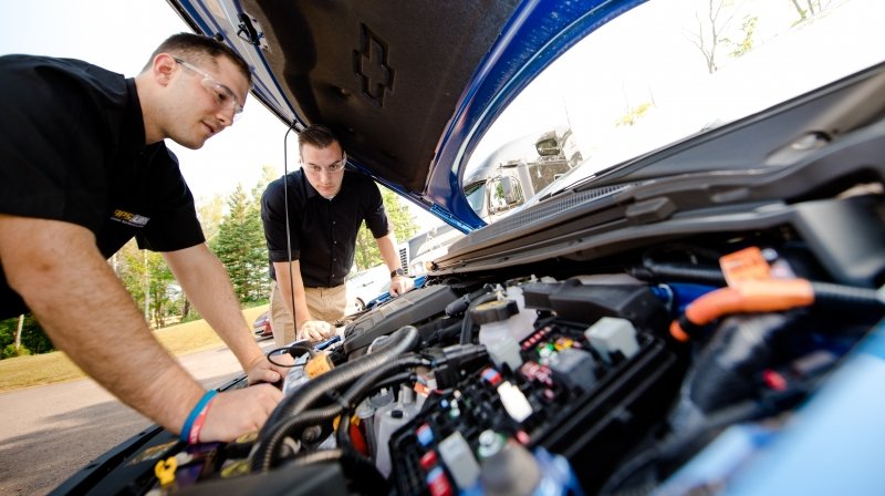 Two people working under the hood of a car.