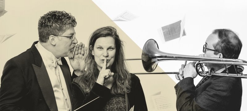 A music conductor whispering to a woman with her finger over her mouth while a third person plays a trombone.