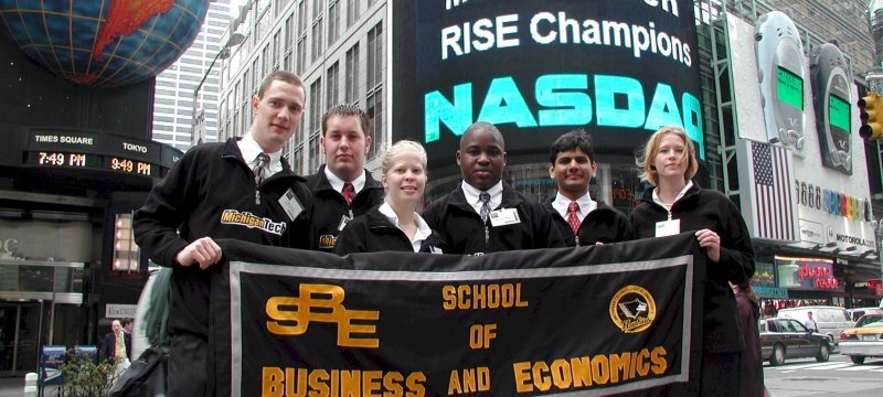 Six students holding a School of Business and Economics banner outside the New York Stock Exchange.