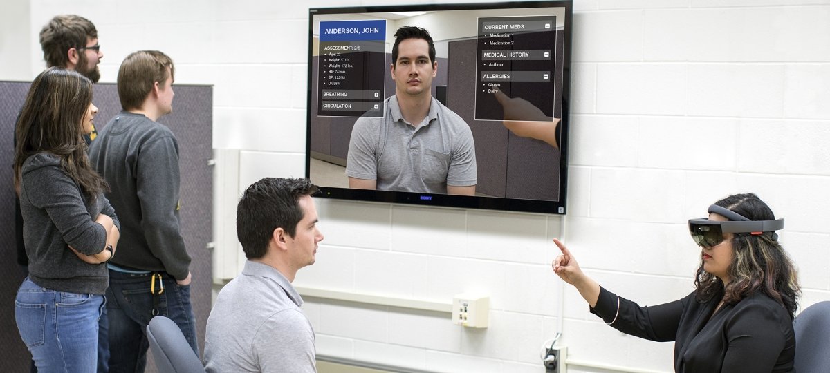 People watching television screen while another person uses virtual reality headset.