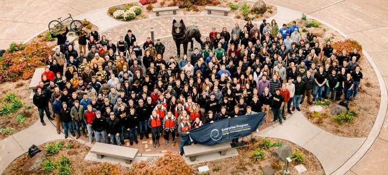 Students in the Enterprise Program pose for a photo around the Husky Statue.