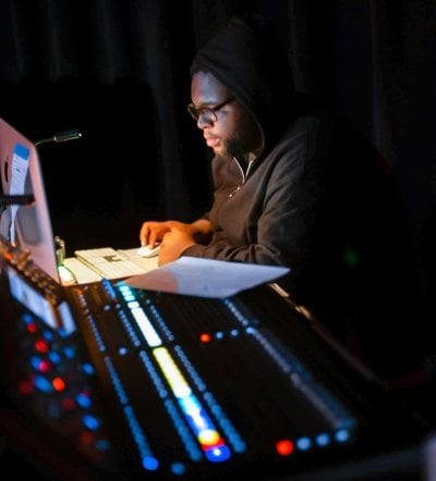 Student working at a computer next to the sound board.