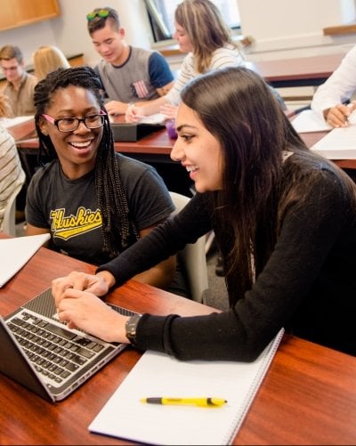 Two students working at a laptop in a classroom.