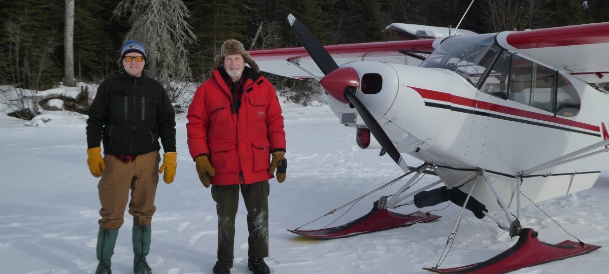 Two men standing next to the skiplane.