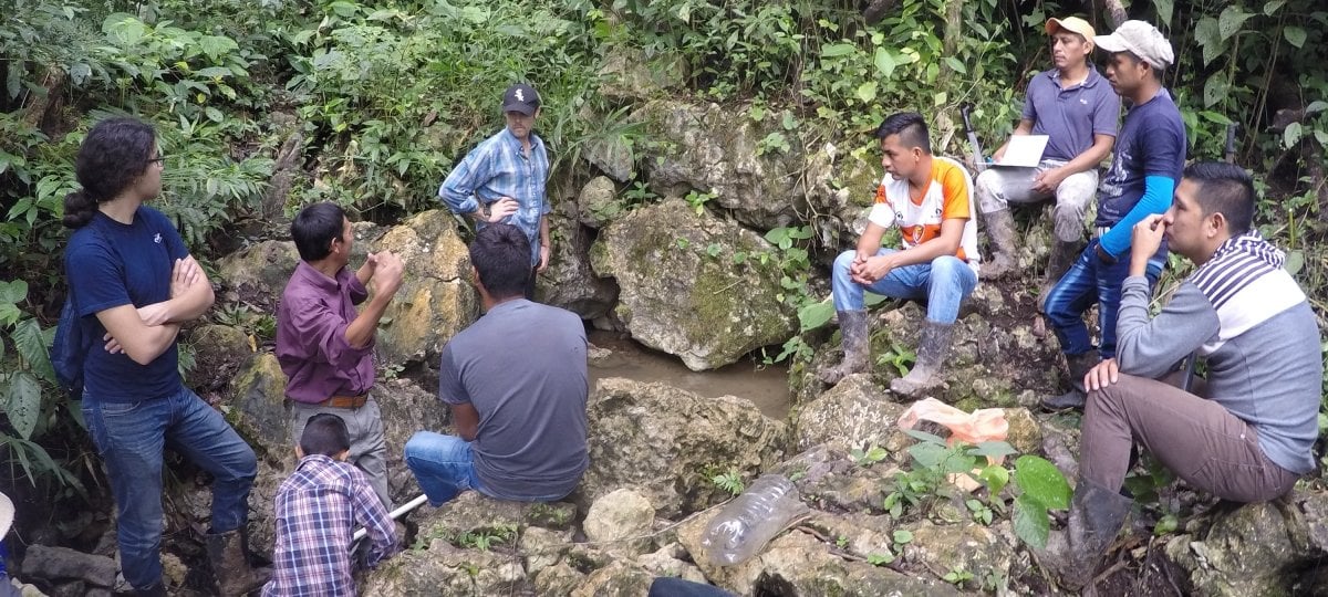 People sitting on rocks around a spring talking.