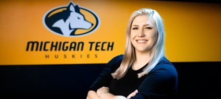 Kaitlyn Roose stands in front of the Husky Logo in the Student Development Complex. A former college athlete at Gannon University, Roose is a PhD student in the Department of Cognitive and Learning Sciences, but is director of Michigan Tech's new Varsity Esports program.