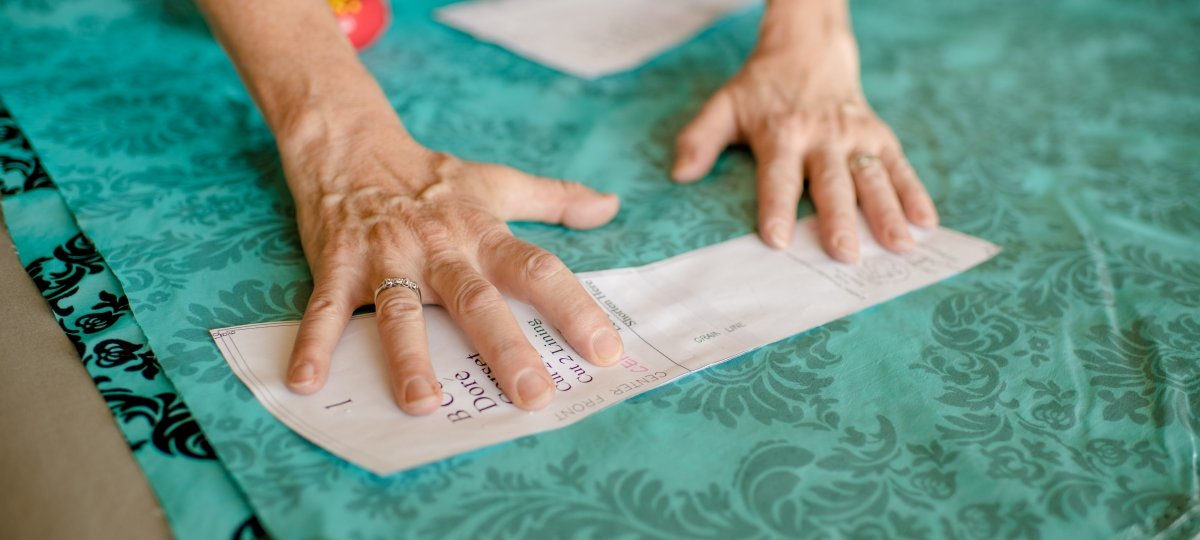 Hands holding a pattern reading center and front on a bolt of damask cloth.