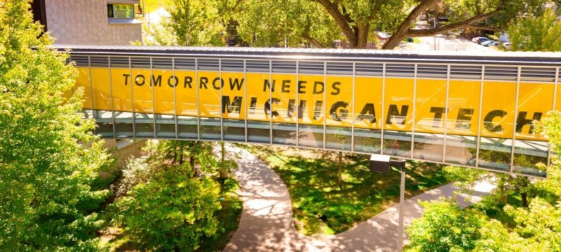 Tomorrow Needs Michigan Tech window wrap on the bridge between Rekhi Hall and the Library.