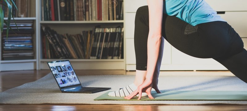 A person doing a yoga pose while watching a video on a laptop.