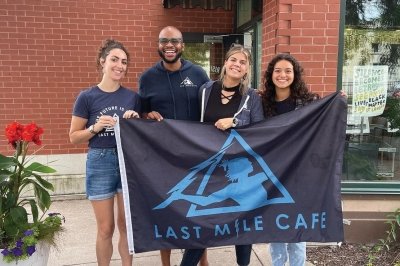 Arick Davis and three employees holding a Last Mile Cafe flag.