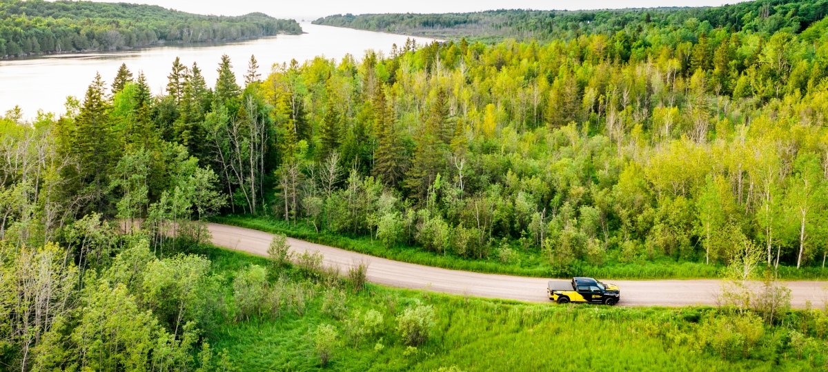 Drone view of a truck driving on a road through the woods.