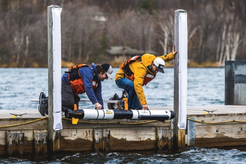 Two people lowering IVER 3 into the water from a dock.