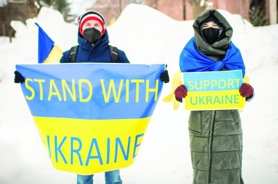 Two people standing outside holding Stand With Ukraine and Support Ukraine signs.