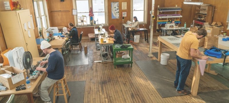 Chicken Tramper employees working in the shop at tables and sewing machines.