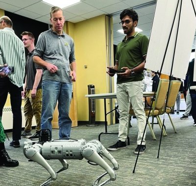 Student demonstrating 4-legged robot during a poster session.