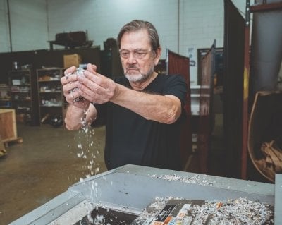 Ezra Bar-Ziv sprinkling a handful of shredded plastic into a machine.