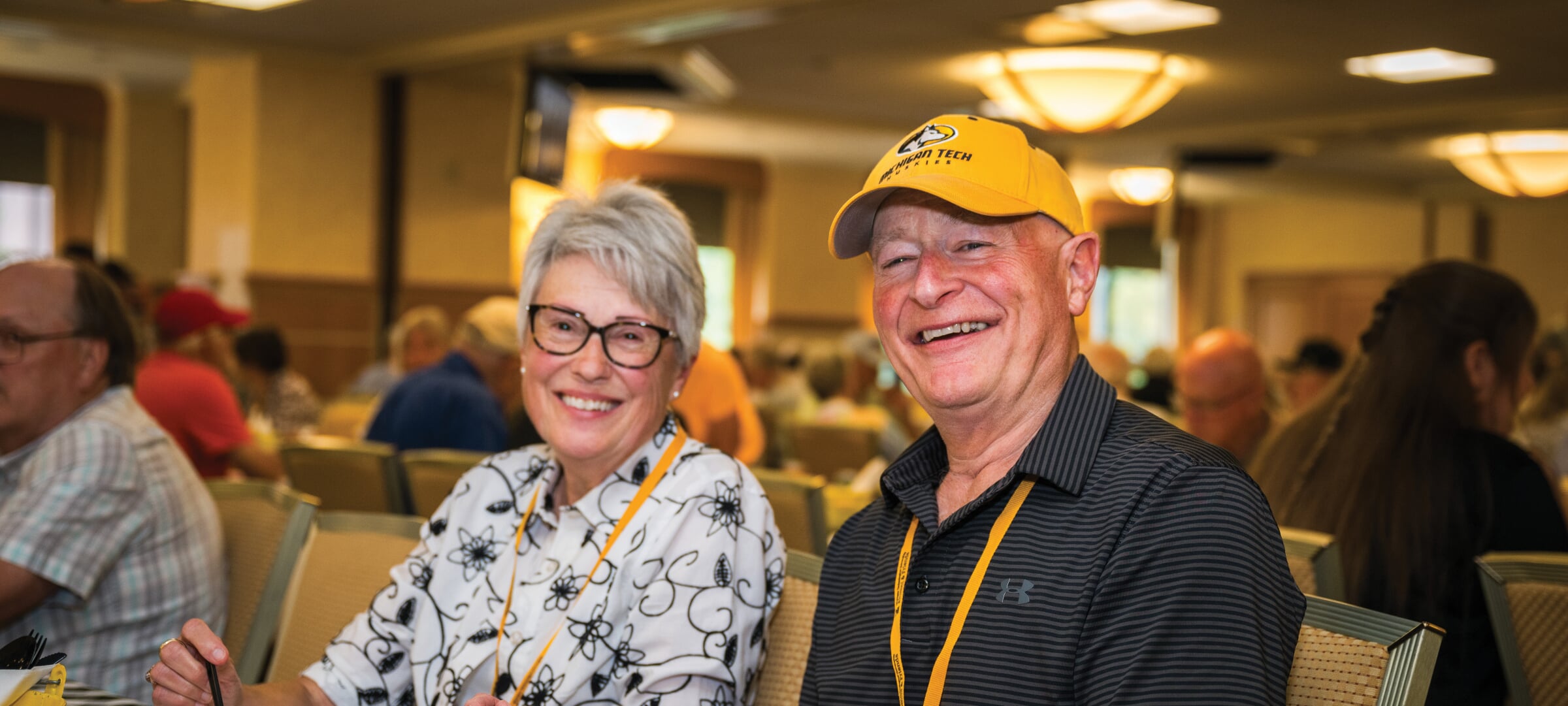 Two alumni at a table eating pasties.