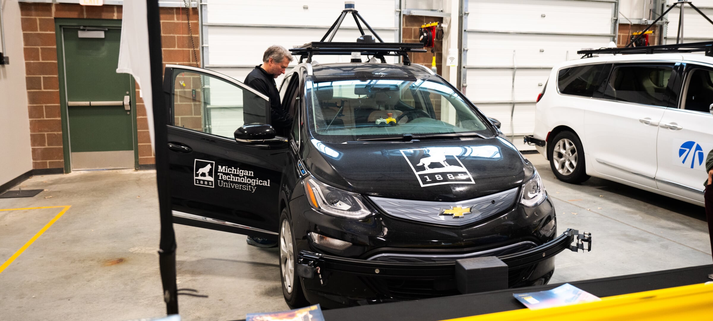 Person standing in an open door of a black car with Michigan Tech logos on it.