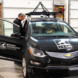 Researcher standing in an open door of a black car with Michigan Tech logos on it.