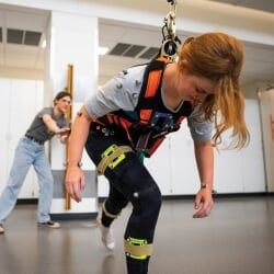 Researcher observing a test subject falling forward while wearing a harness.