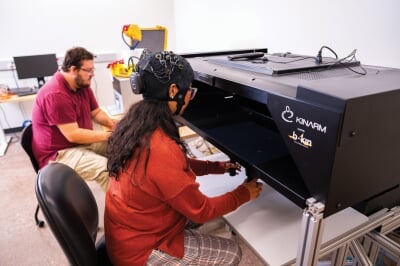 Research observes person with electrode cap on while they are manipulating another machine.
