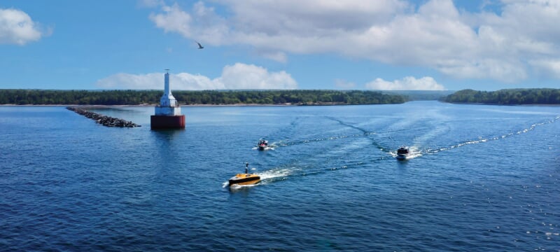 Three boats in the water going past a lighthouse.