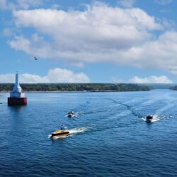 Three boats in the water going past a lighthouse.
